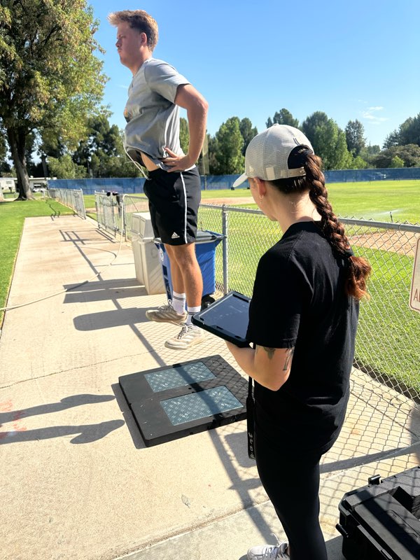 A coach with a tablet next to force plates on the sideline.