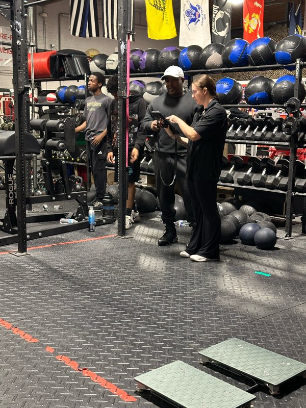 A coach recording results on a tablet while athletes wait to test on the force plates.